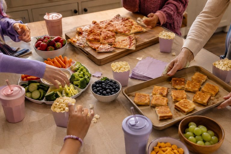 Children reaching for pizza, fruit, vegetables and popcorn at an easy sleepover food table