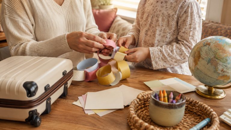 A parent and child make a paper countdown chain beside a small suitcase and globe.